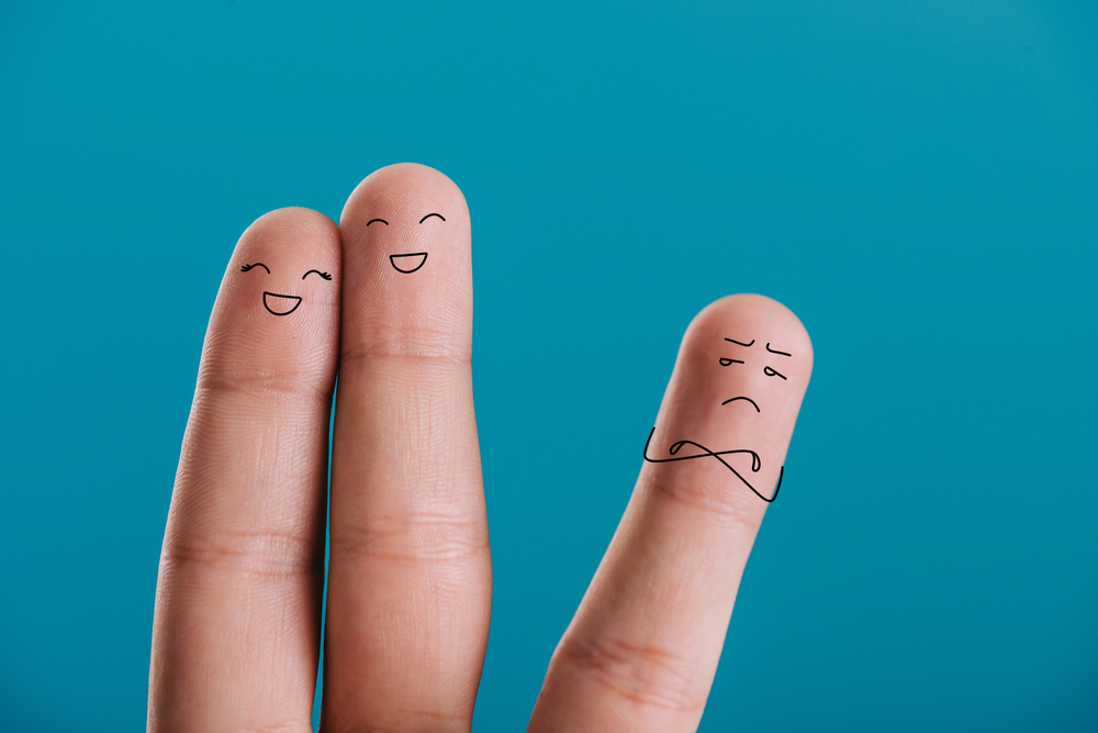 Two fingers side by side showing happy faces while another one stands on the side showing dissatisfaction – symbolizing polyamory under duress (PUD)